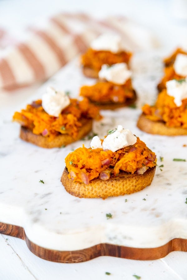 A marble and wood board with sweet potato canapes topped with ricotta.