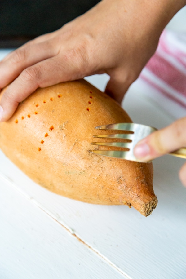 Hands piercing a sweet potato with a fork.