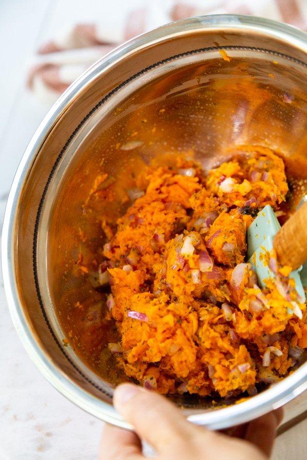 A hand stirring sweet potato and spices together in a bowl