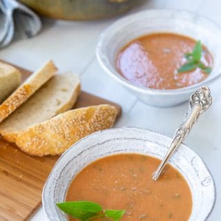 Two bowls of tomato soup with sliced bread on a board.