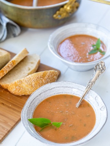 Two bowls of tomato soup with sliced bread on a board.