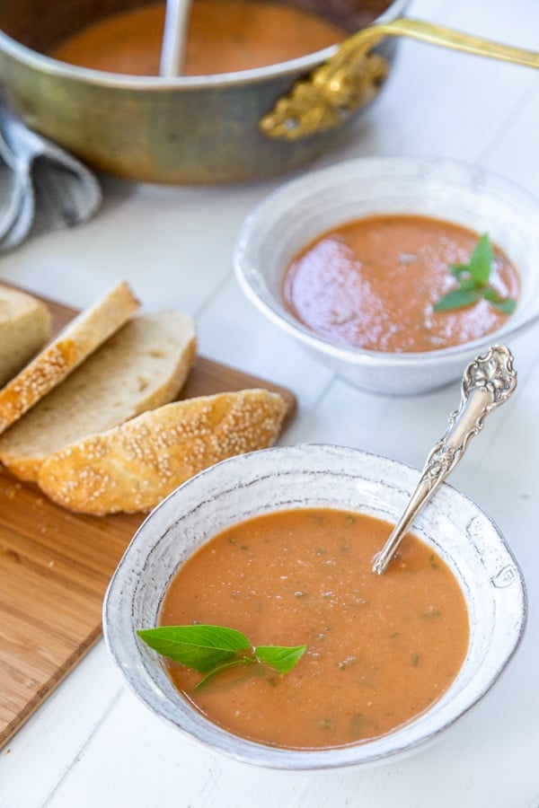 Two bowls of tomato soup with sliced bread on a board.