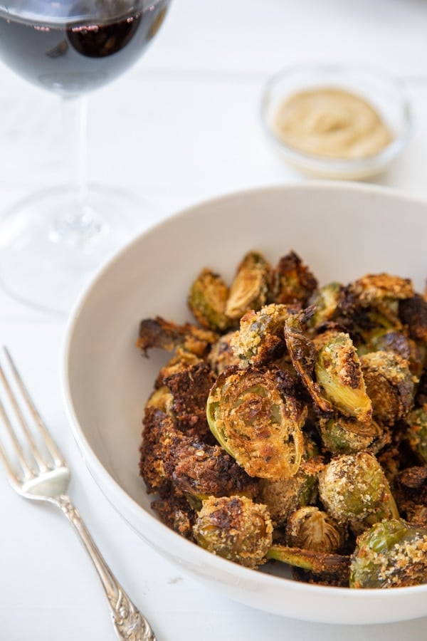 Crispy Brussels sprouts in a white bowl with a silver fork next to the bowl.