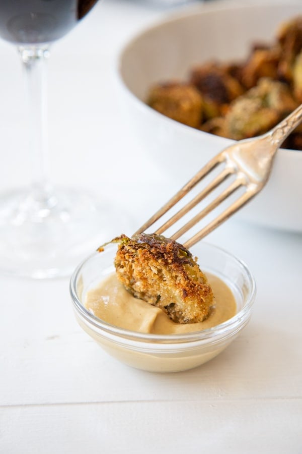 A silver fork dipping a crispy Brussels sprout into a bowl of dip. 