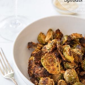 A white bowl of breaded Brussels sprouts with black text that says Maple Breaded Sprouts at the top right of the picture.