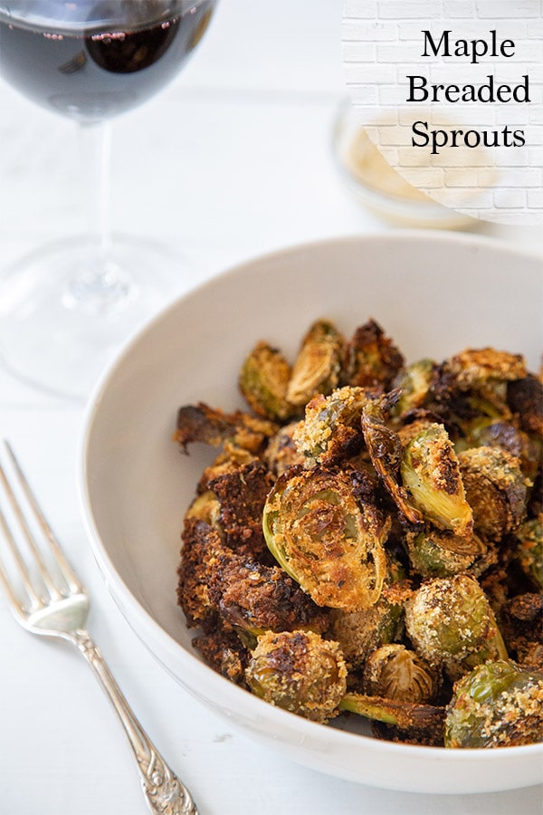 A white bowl of breaded Brussels sprouts with black text that says Maple Breaded Sprouts at the top right of the picture.