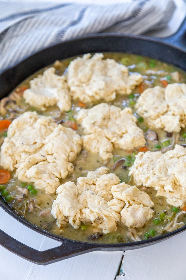 An iron skillet with chicken and vegetable stew and uncooked drop biscuits over the stew.