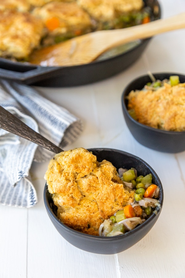 A skillet with chicken and biscuits and 2 black bowls of the recipe. 