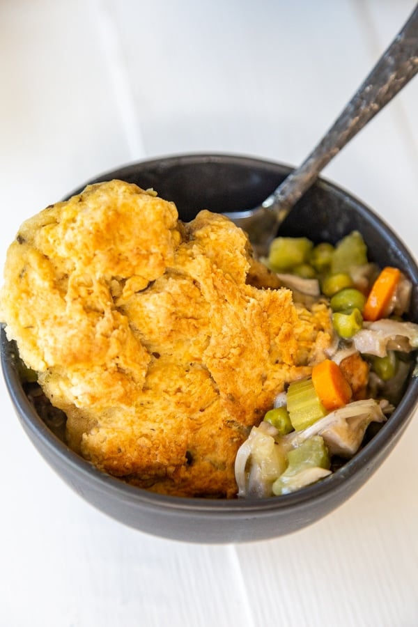 A black bowl with chicken and biscuits and a fork in the bowl.