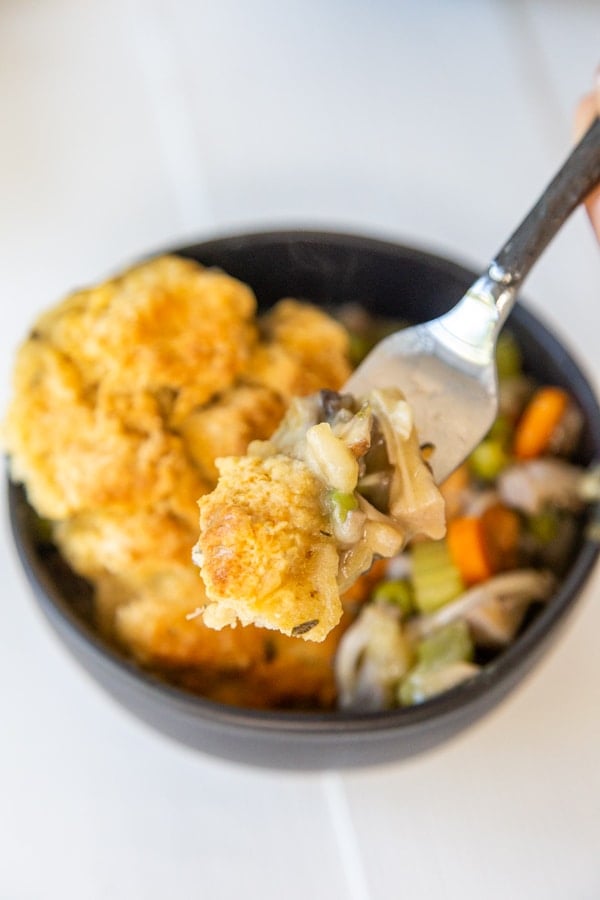 A fork taking a piece of chicken and biscuits from a black bowl. 