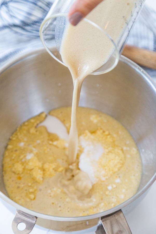 A measuring cup of milk being poured into cornmeal and flour.