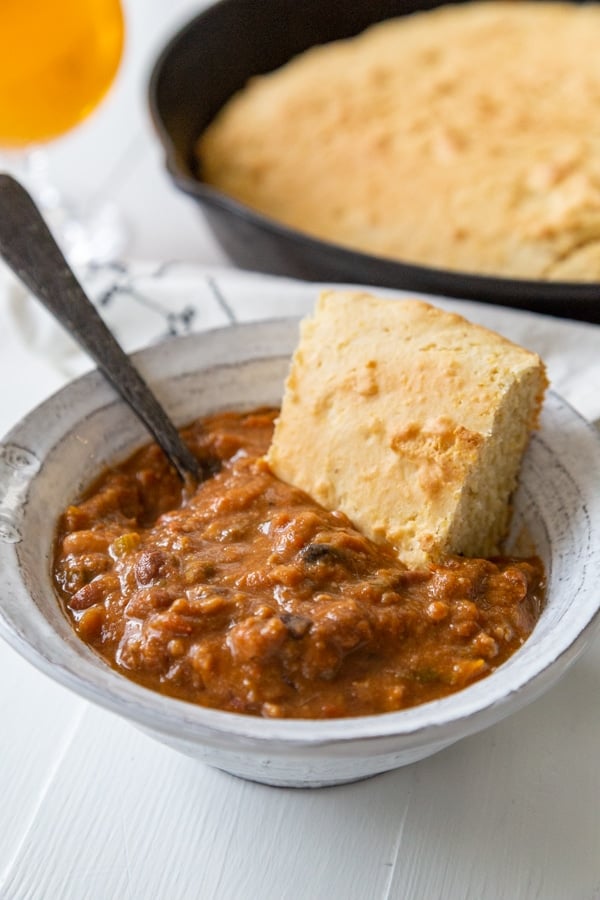 A bowl of chili with a slice of cornbread and a spoon in the bowl. 