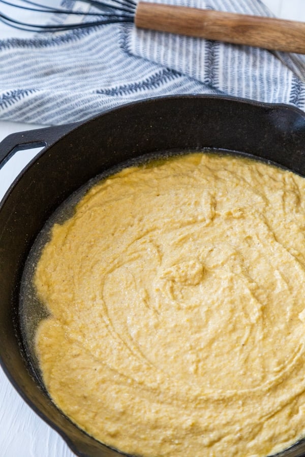 Cornbread batter spread evenly in an iron skillet.