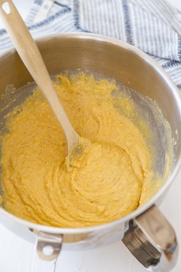 Cornbread batter in a silver mixing bowl with a wooden spoon stirring the batter.