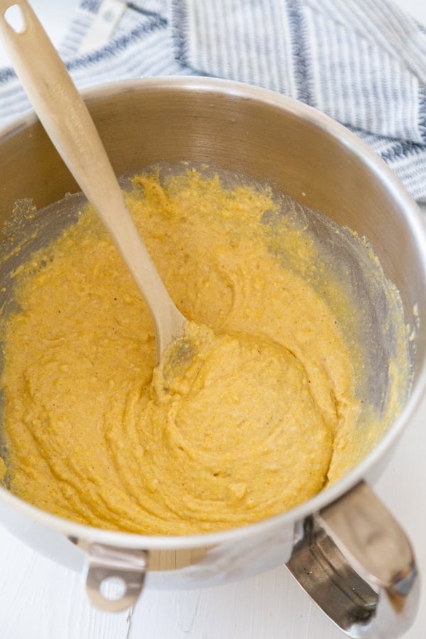 Cornbread batter in a silver mixing bowl with a wooden spoon stirring the batter.