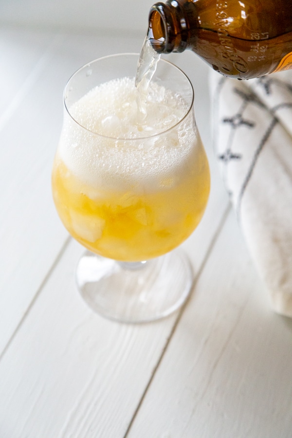 A bottle of ginger beer being poured into a glass of ice and rum.