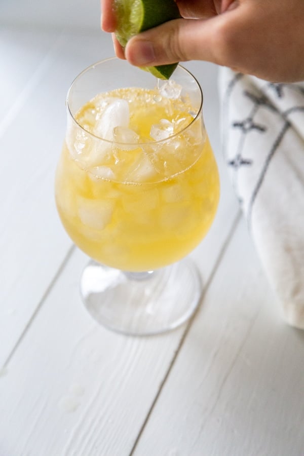 A hand squeezing a lime over a glass of ginger beer and rum.