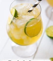 A glass of a dark and stormy cocktail with lime wheels and a black and white straw.