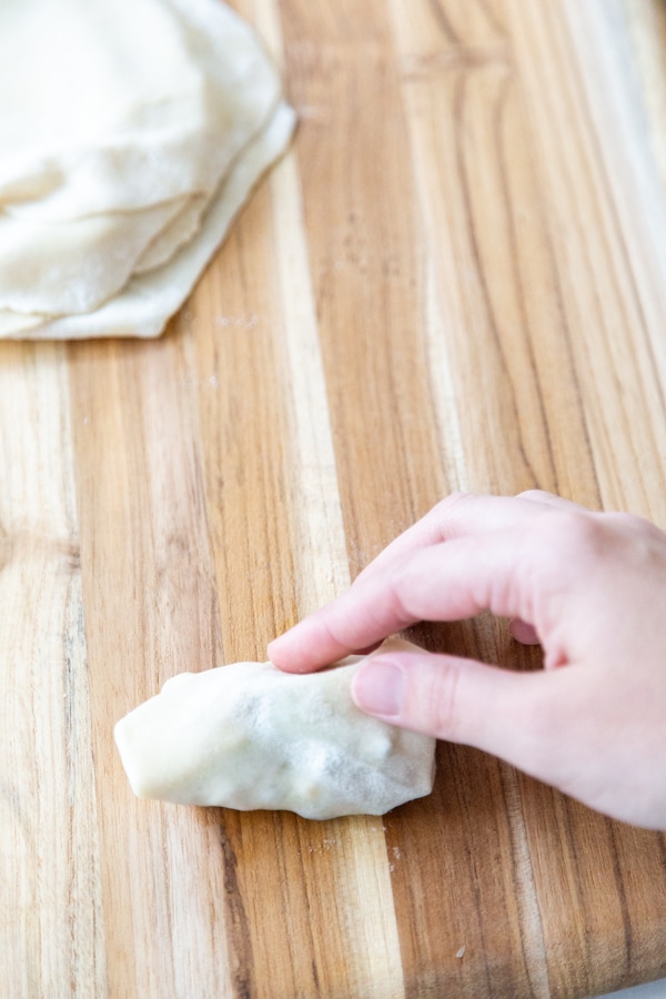 A hand folding an egg roll on a wood board.