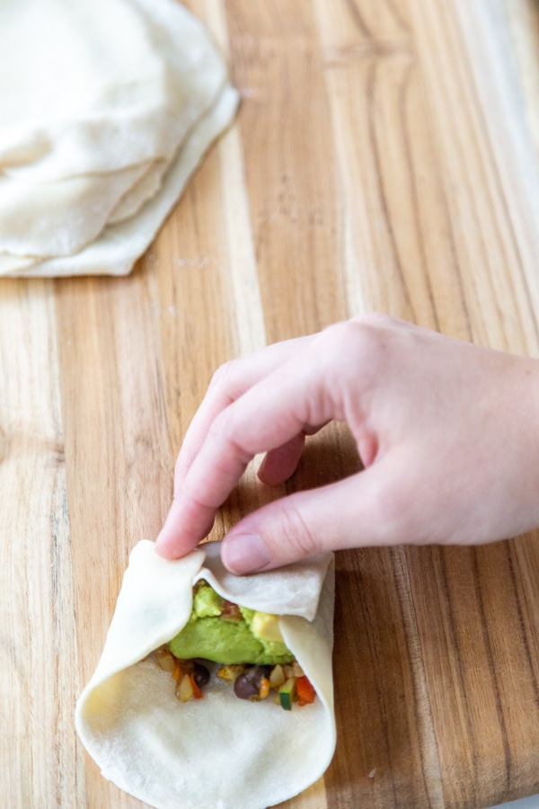 A hand folding a veggie filled egg roll.