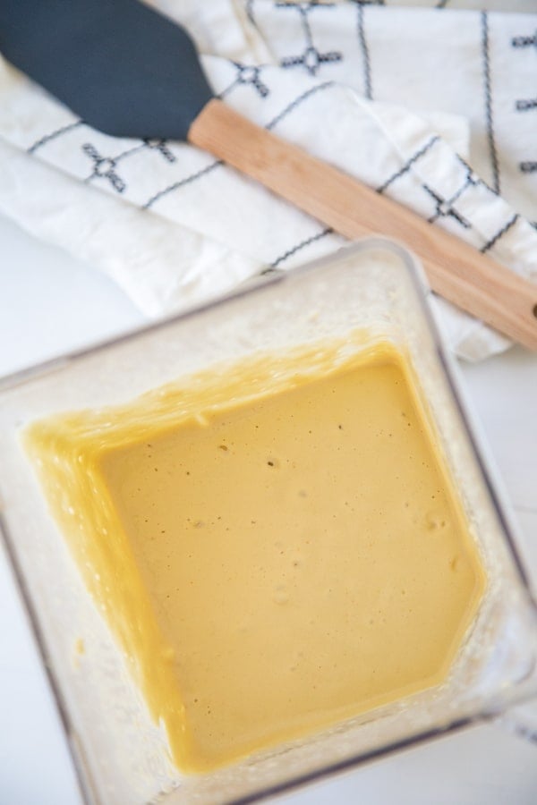 A blender pitcher with cheese sauce and a spatula next to the pitcher. 