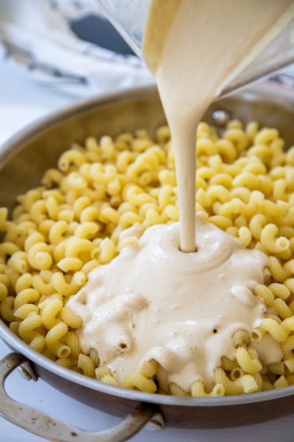 A round pan with noodles and cheese sauce being poured on top of the noodles.