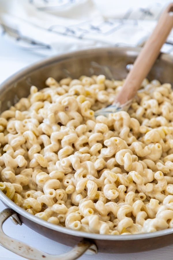 A wooden spoon stirring cheese sauce and noodles together in a round pan.