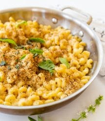 A copper pan of baked mac 'n' cheese with a bread crumb topping and fresh herbs.