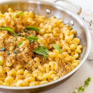 A copper pan of baked mac 'n' cheese with a bread crumb topping and fresh herbs.