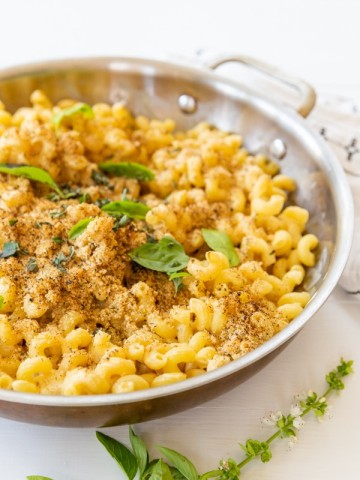A copper pan of baked mac 'n' cheese with a bread crumb topping and fresh herbs.