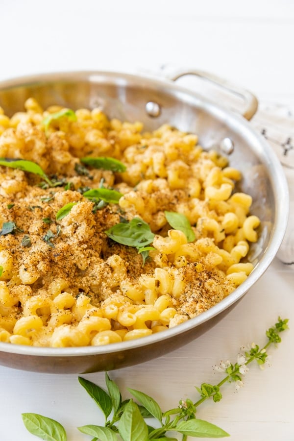 A copper pan of baked mac 'n' cheese with a bread crumb topping and fresh herbs.