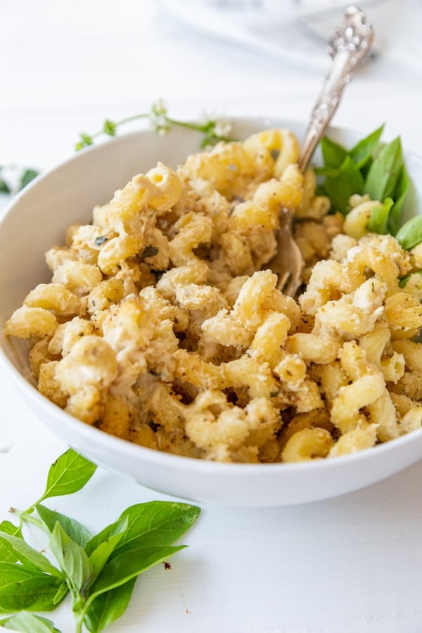 A white bowl with vegan mac 'n' cheese and a silver fork digging in to the dish. 