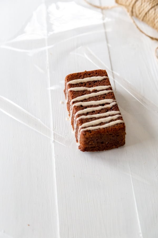 A mini chocolate loaf cake with icing on a square of clear cellophane.