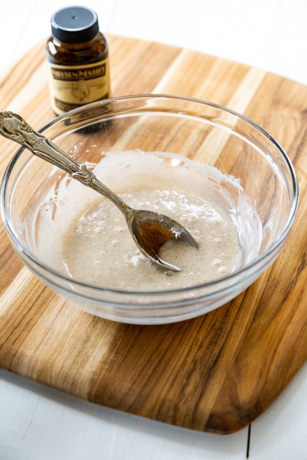 A clear glass bowl of vanilla icing with a spoon in the bowl.
