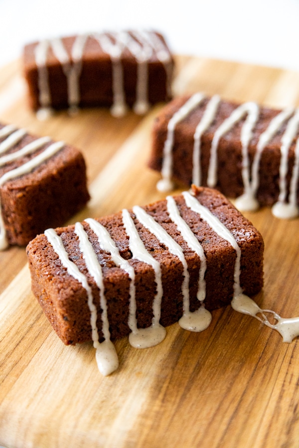4 mini chocolate cake loaves with icing drizzled over on a wood board. 