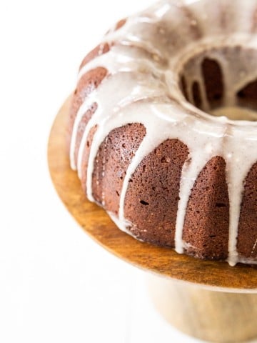 Half of a chocolate bundt cake with icing drizzled down the sides on a wood cake plate.