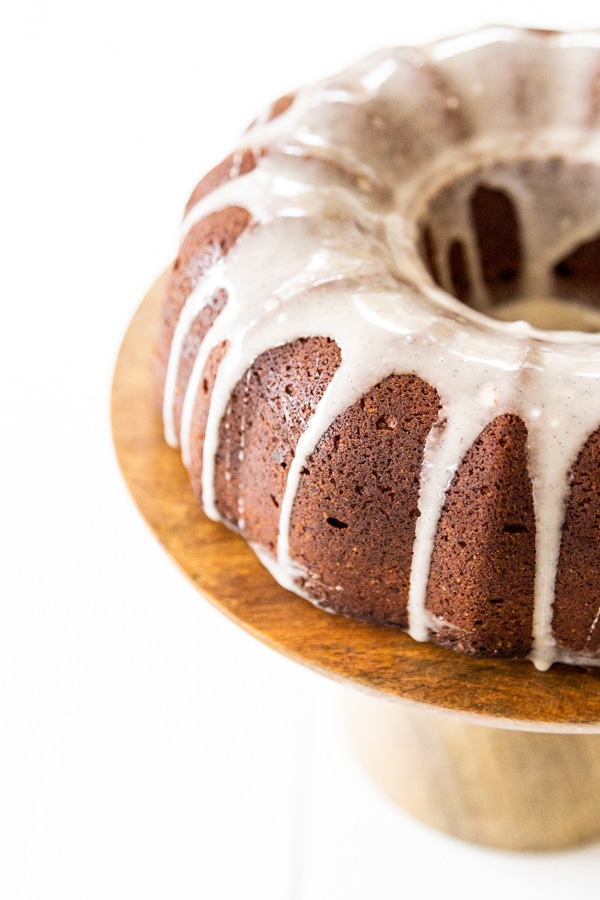 Half of a chocolate bundt cake with icing drizzled down the sides on a wood cake plate. 