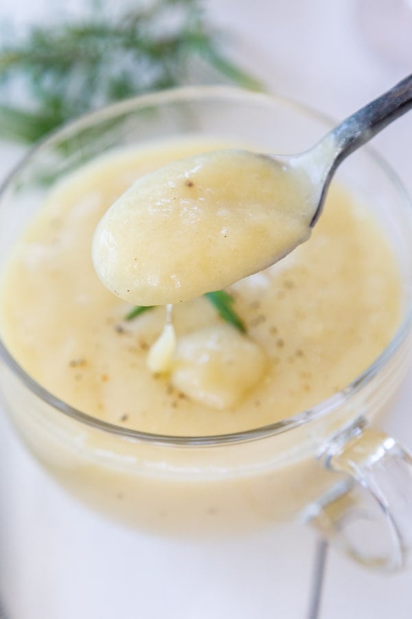 A spoonful of potato soup being held over a clear glass mug of the soup.