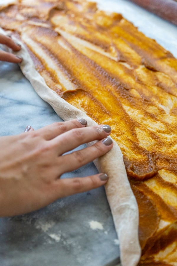 Hands rolling a rectangular piece of dough with pumpkin filling.