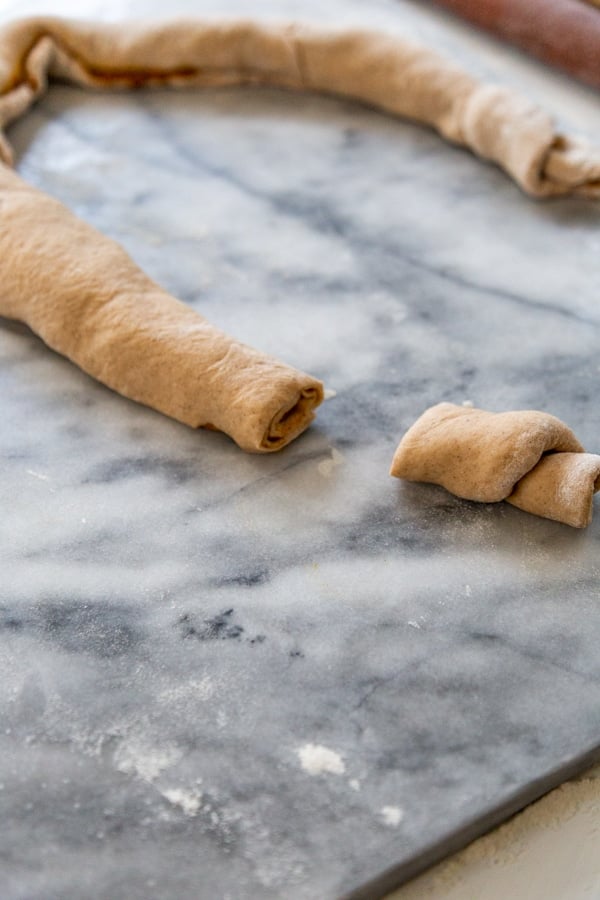 A tube of dough with pumpkin filling on a marble surface with slices cut out of it.