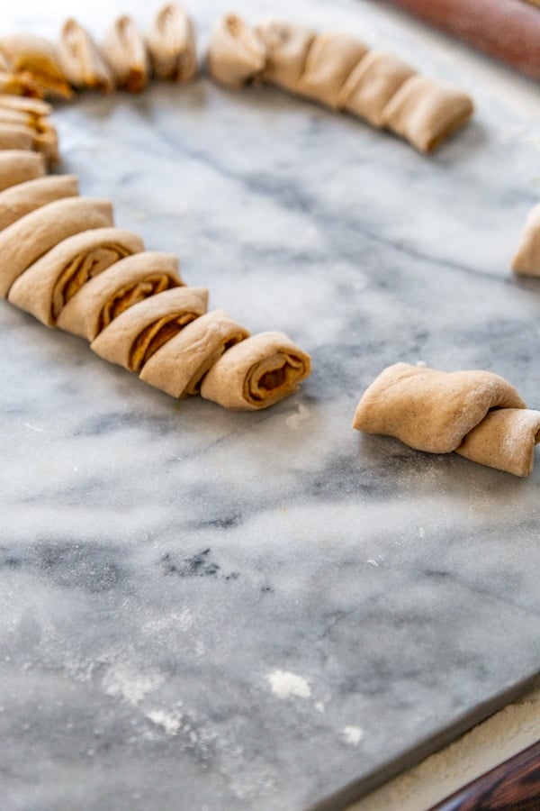 Sliced dough for pumpkin cinnamon rolls on a marble surface.