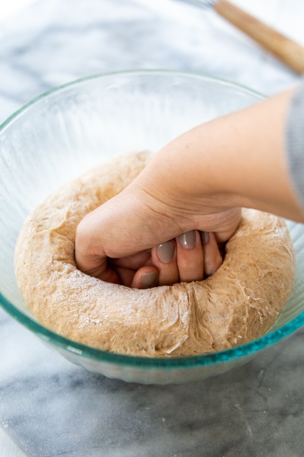 A hand punching risen dough in a glass bowl.