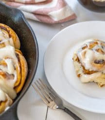 An iron skillet with pumpkin cinnamon rolls and a white plate with a roll on it.
