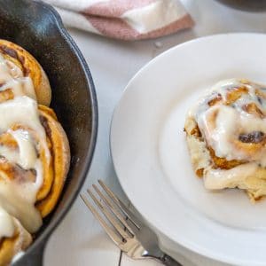 An iron skillet with pumpkin cinnamon rolls and a white plate with a roll on it.