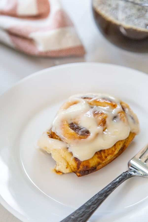 A white plate with a cinnamon roll and a silver fork. 