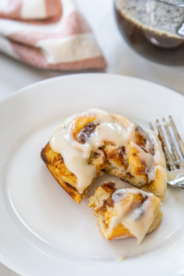 A white plate with a fork that cut into a cinnamon roll. 