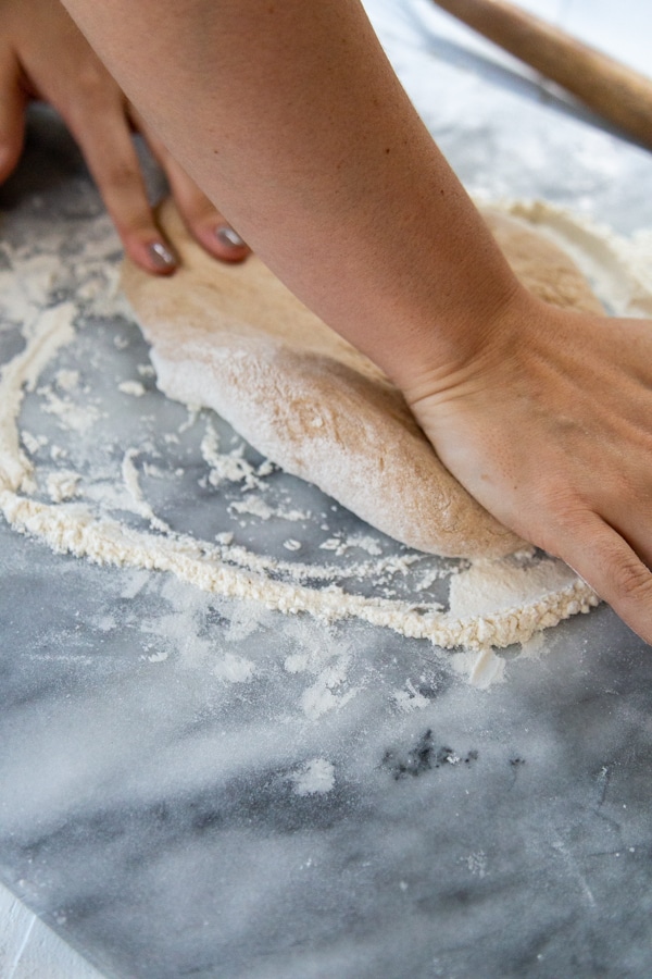 Two hands stretching dough on a floured marble surface.