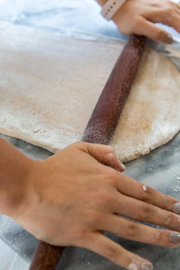 Hands rolling dough with a wood rolling pin.