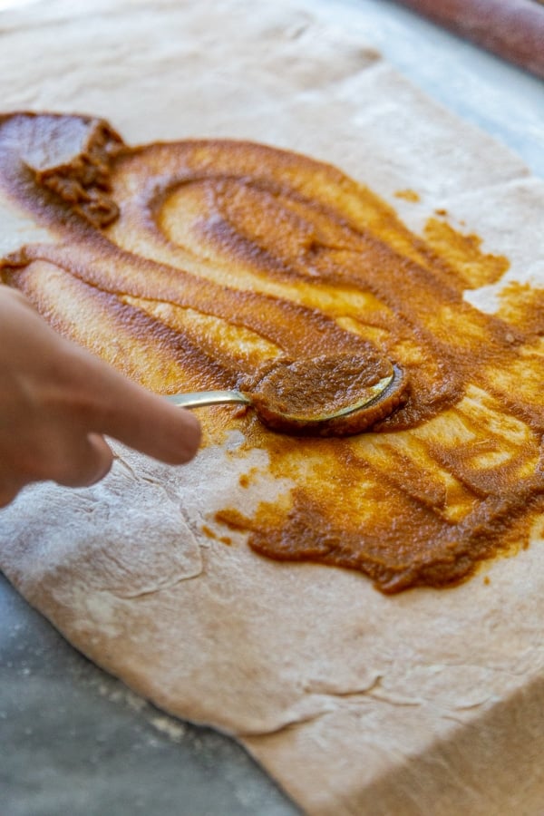 A hand spreading pumpkin filling on a rectangular piece of dough.