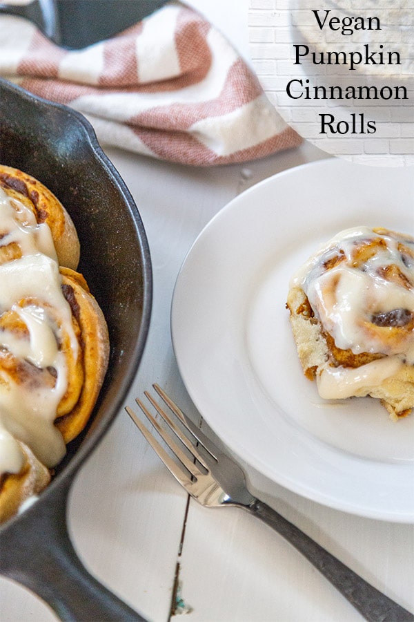 An iron skillet with cinnamon rolls and a white plate with a roll.